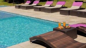 A poolside area with lounge chairs and umbrellas, a wooden cabin, and a forested backdrop.