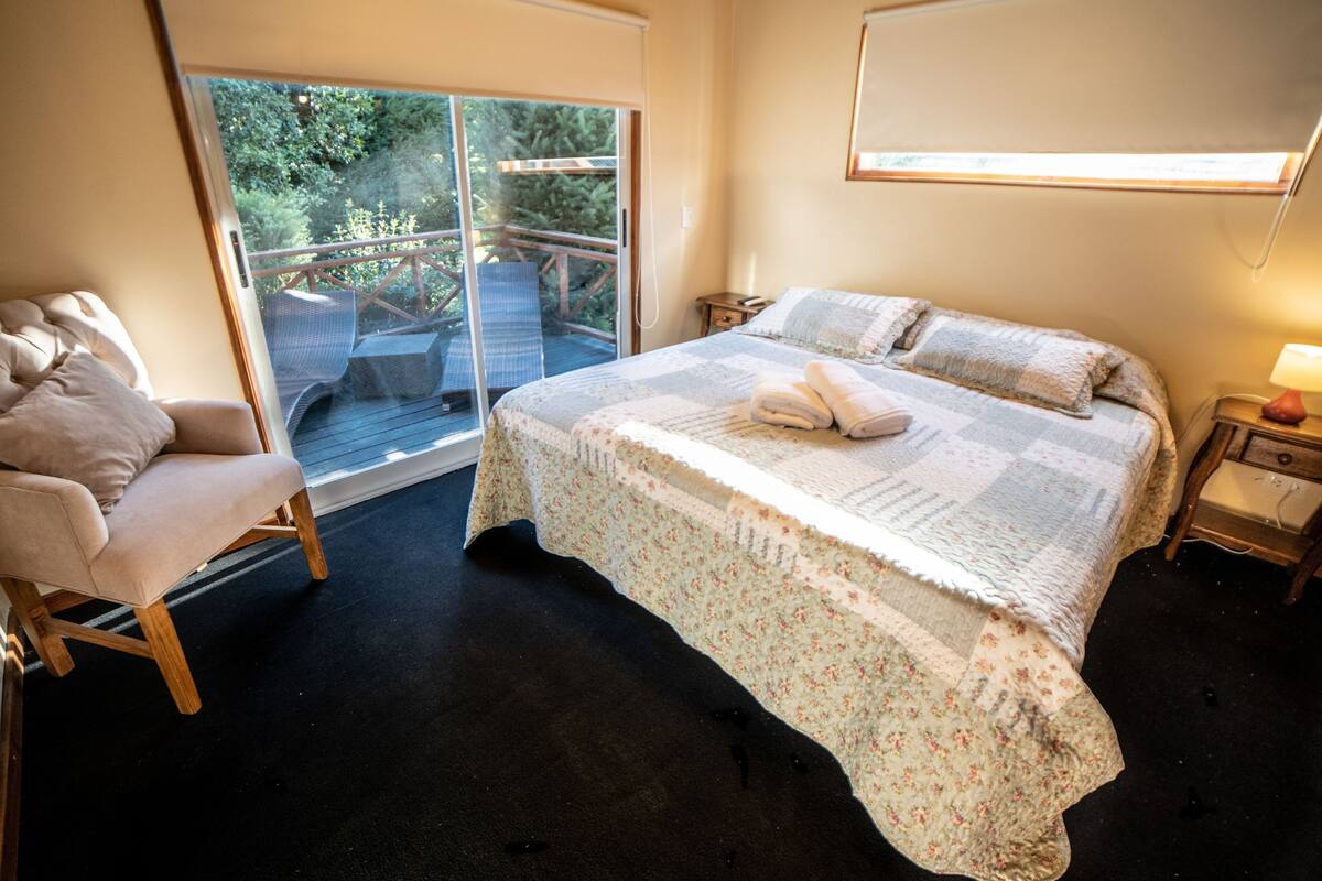 Une chambre avec un grand lit, une chaise, une table de chevet et une fenêtre donnant sur un paysage verdoyant.