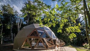 A geodesic dome structure with a wooden deck and two wicker chairs.