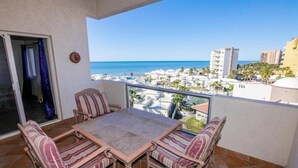 Un balcon avec une table et des chaises, offrant une vue sur la plage et les bâtiments environnants.