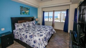 Une chambre avec un lit, un ventilateur de plafond, une fenêtre avec des rideaux et une vue sur la mer.