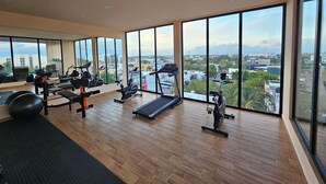 Une salle de sport moderne équipée de machines de cardio, de poids libres et dotée d’une grande fenêtre offrant une vue sur la ville.