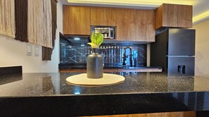 Une cuisine moderne dotée d’un plan de travail en granit noir, de meubles en bois et d’une hotte en acier inoxydable.