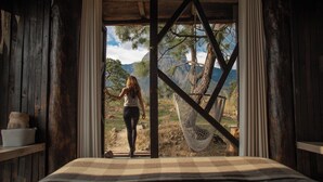 Une pièce rustique en bois, avec un lit, un hamac et une vue sur un paysage montagneux.