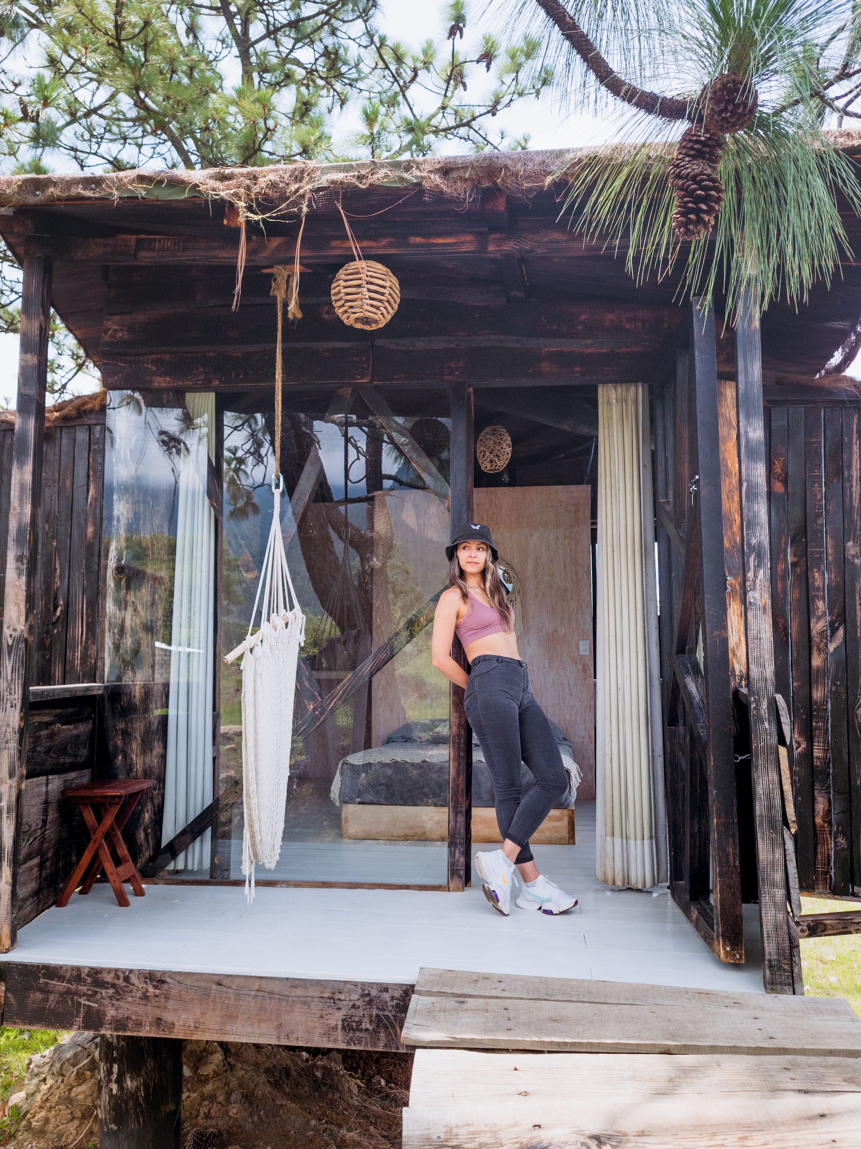A rustic wooden cabin with a hammock, a bed, and a small table.