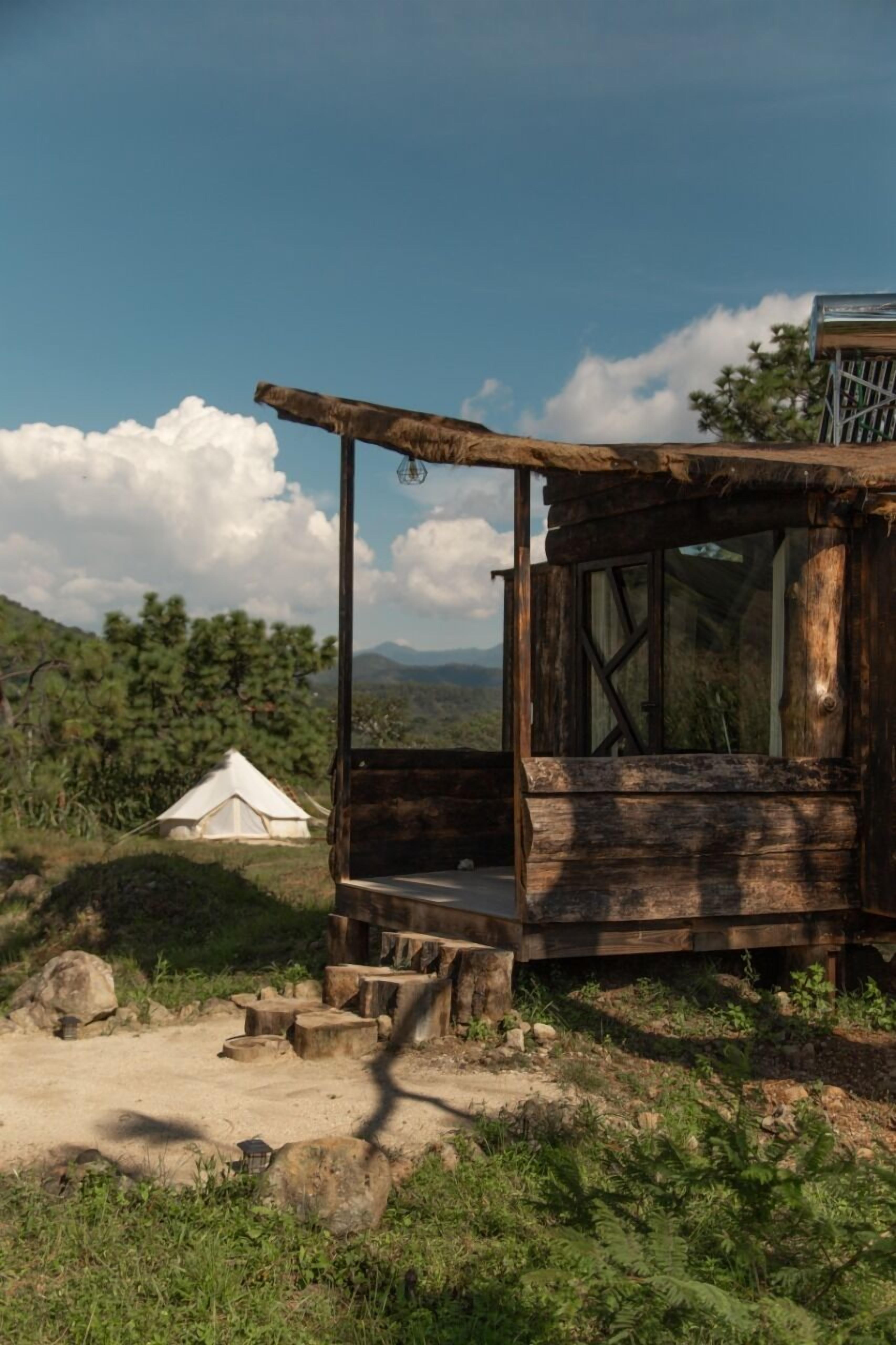 Une structure rustique en bois, dotée d’une grande fenêtre, avec une tente en arrière-plan et une vue dégagée sur le paysage environnant.