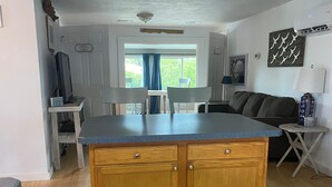 A kitchen with wooden cabinets, a blue countertop, and a dining area with a table and chairs. - Charming waterfront 2 bedroom with bonus room that sleeps 8 in scenic Cedar Key (Cedar Key)