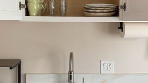 A kitchen with a white countertop, a stainless steel faucet, and a cabinet above holding dishes and glassware.
