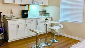 A compact kitchen with white cabinets, a coffee machine, and two bar stools.