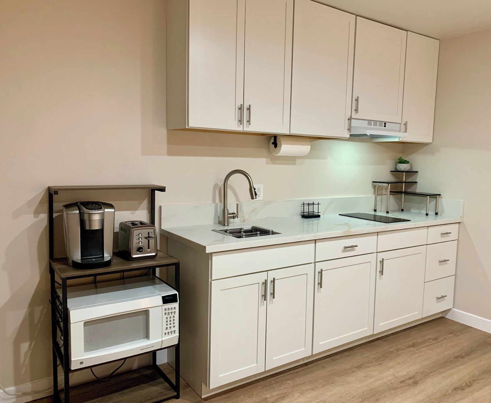 A compact kitchen with white cabinets, a built-in microwave, a coffee maker, and a sink.