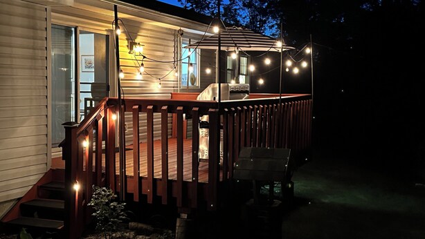 Una terraza de madera con luces colgantes, un espacio cubierto y una escalera que lleva a una puerta.