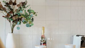 A modern kitchen with white cabinets, a white tiled backsplash, a vase with green foliage, a bottle of champagne, and two white bowls on the counter. - Couples Retreat - Million Dollar Wakatipu Views! (Queenstown)