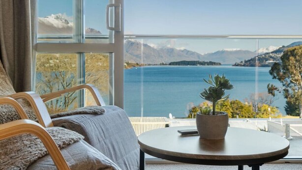A room with a view of a lake and mountains, a round table with a potted plant, and a sofa with a blanket. - Couples Retreat - Million Dollar Wakatipu Views! (Queenstown)
