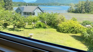 A view from a window of a house with a lawn, trees, and mountains in the background. - Fletchers Cabin (Ucluelet)