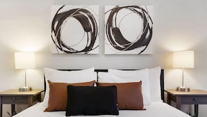 Camera d'albergo con un letto, due comodini, due lampade e due quadri astratti alle pareti.