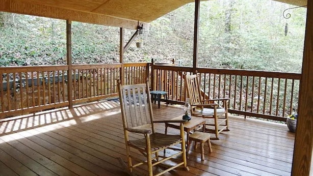 A wooden deck with a table and chairs, surrounded by a wooden railing, overlooking a forested area.