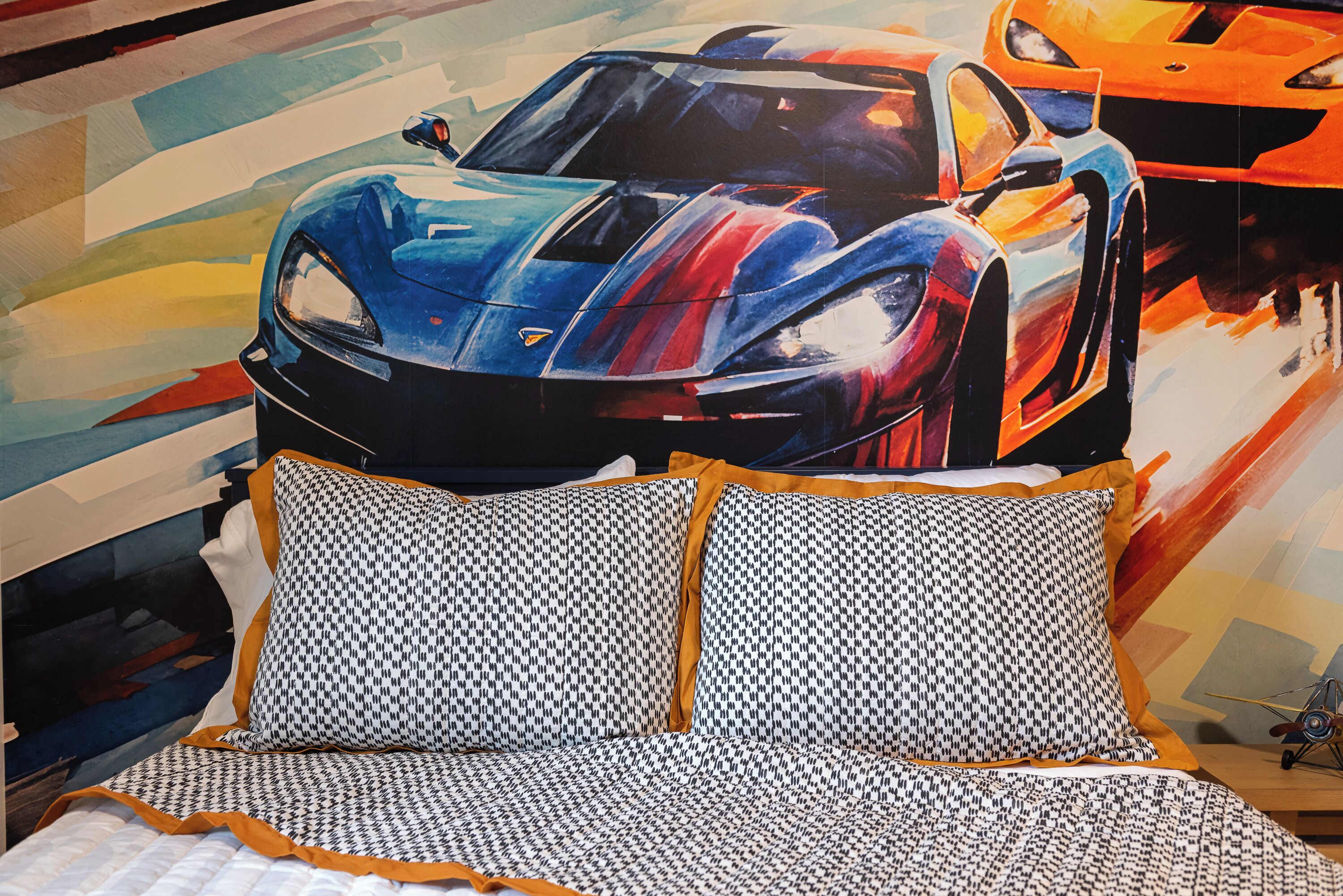 A bed with patterned pillows and a wall mural of a sports car.