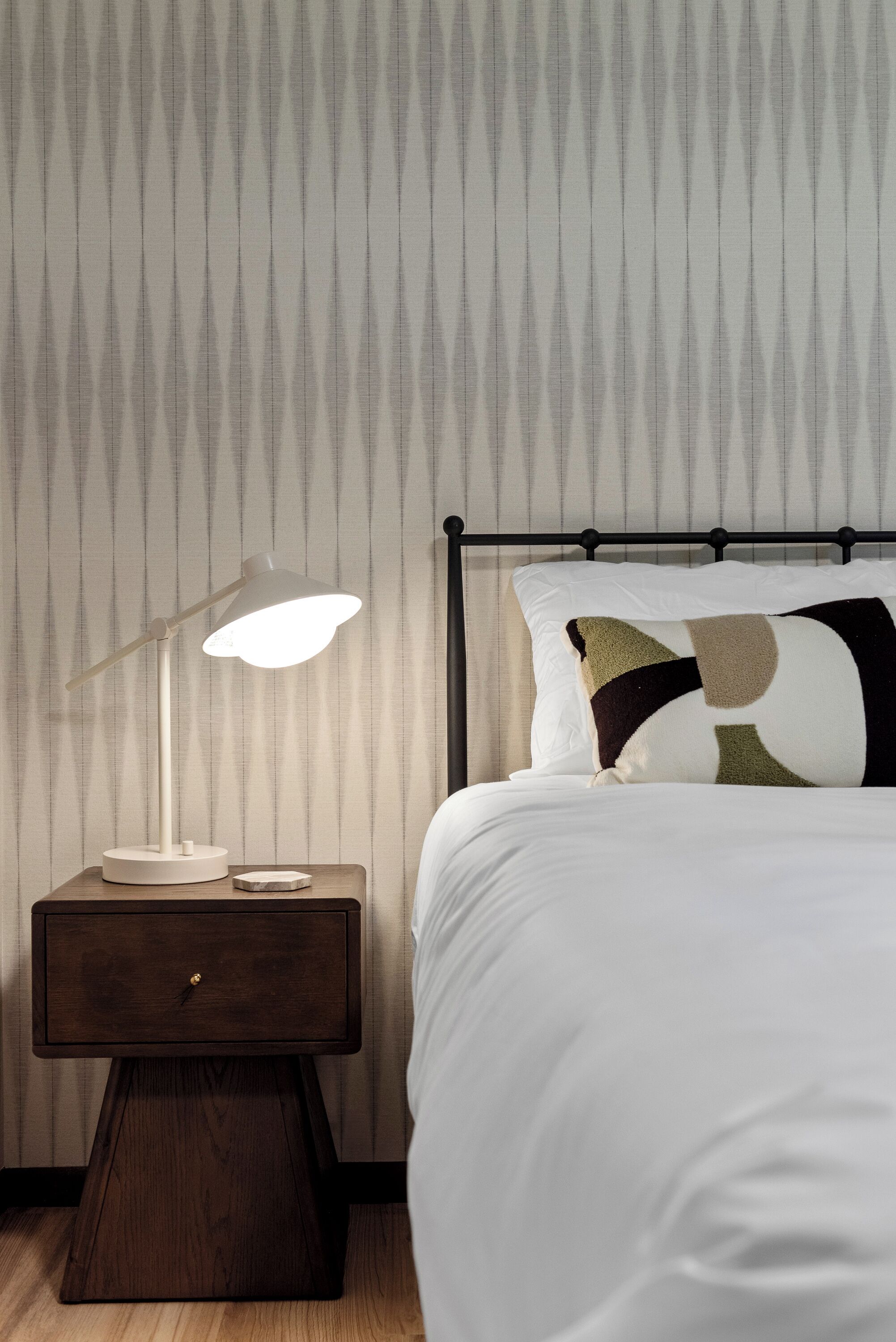 Un letto rifatto con cura, un cuscino decorato, un comodino con una lampada e un piccolo tavolo in legno.