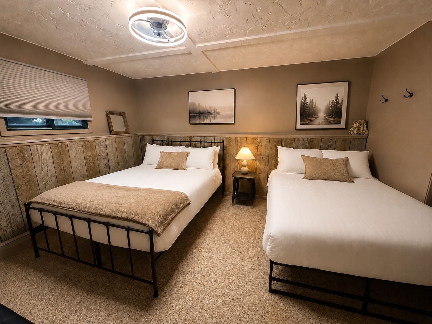 Een hotelkamer met twee bedden, een plafondventilator, een lamp en ingelijste foto’s aan de muur.