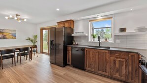 Una cocina moderna con armarios de madera, un refrigerador negro y un comedor con mesa y sillas de madera.
