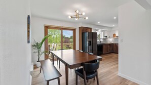 Una cocina moderna con armarios de madera, un refrigerador negro y un comedor con mesa y sillas de madera.