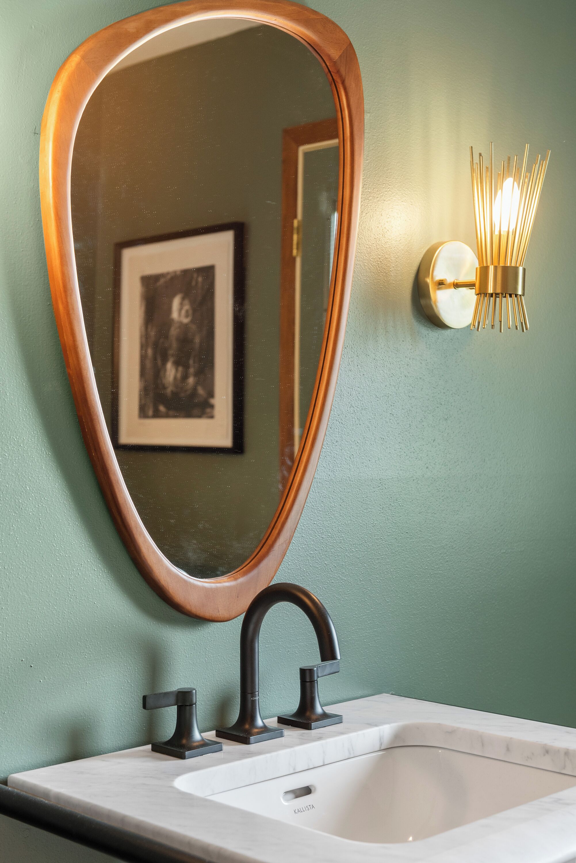 A bathroom with a large oval mirror, a modern faucet, and a wall-mounted light fixture.