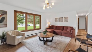 Una sala de estar moderna con un sillón beige, una mesa redonda de centro con una planta, un sofá modular rojo y piso de madera.