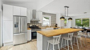 A modern kitchen with white cabinets, stainless steel appliances, a wooden island with bar stools, and pendant lighting.