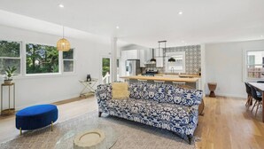 A spacious living area with a patterned sofa, a dining table, and a kitchen in the background.