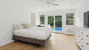 A bedroom with a bed, a desk, a chair, a TV, a ceiling fan, and a view of a swimming pool.