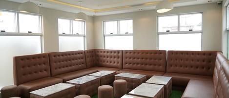 A modern lounge area with a brown leather sectional sofa, multiple ottomans, and marble-topped tables.