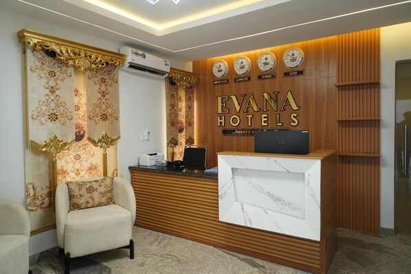 Un área de recepción con un mostrador de madera, un sillón cómodo y una pared con relojes y nombres de ciudades.