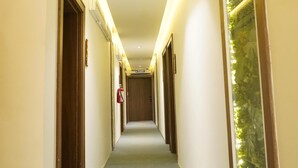 A hotel hallway with a carpeted floor, wooden doors, and a glass wall with greenery. - Evana Hotels (Uyo)
