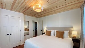 Ein Schlafzimmer mit einem großen Bett, Holzboden, weißen Wänden und einem Spiegel.