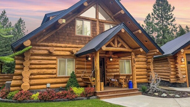 A log cabin with a porch, large windows, and a well-maintained lawn.