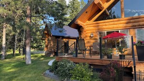 A log cabin with a deck, outdoor seating, and a view of the surrounding forest.