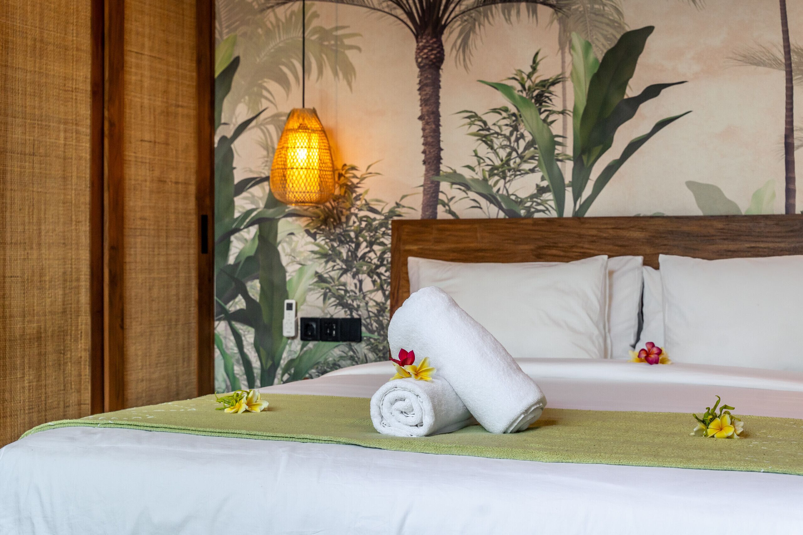 Una habitación de hotel con una cama, un edredón verde, una toalla enrollada y una flor.