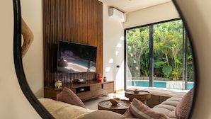 Ein modernes Wohnzimmer mit Fernseher, einer Wand aus Holzpaneelen und einem großen Fenster mit Blick auf einen Pool.