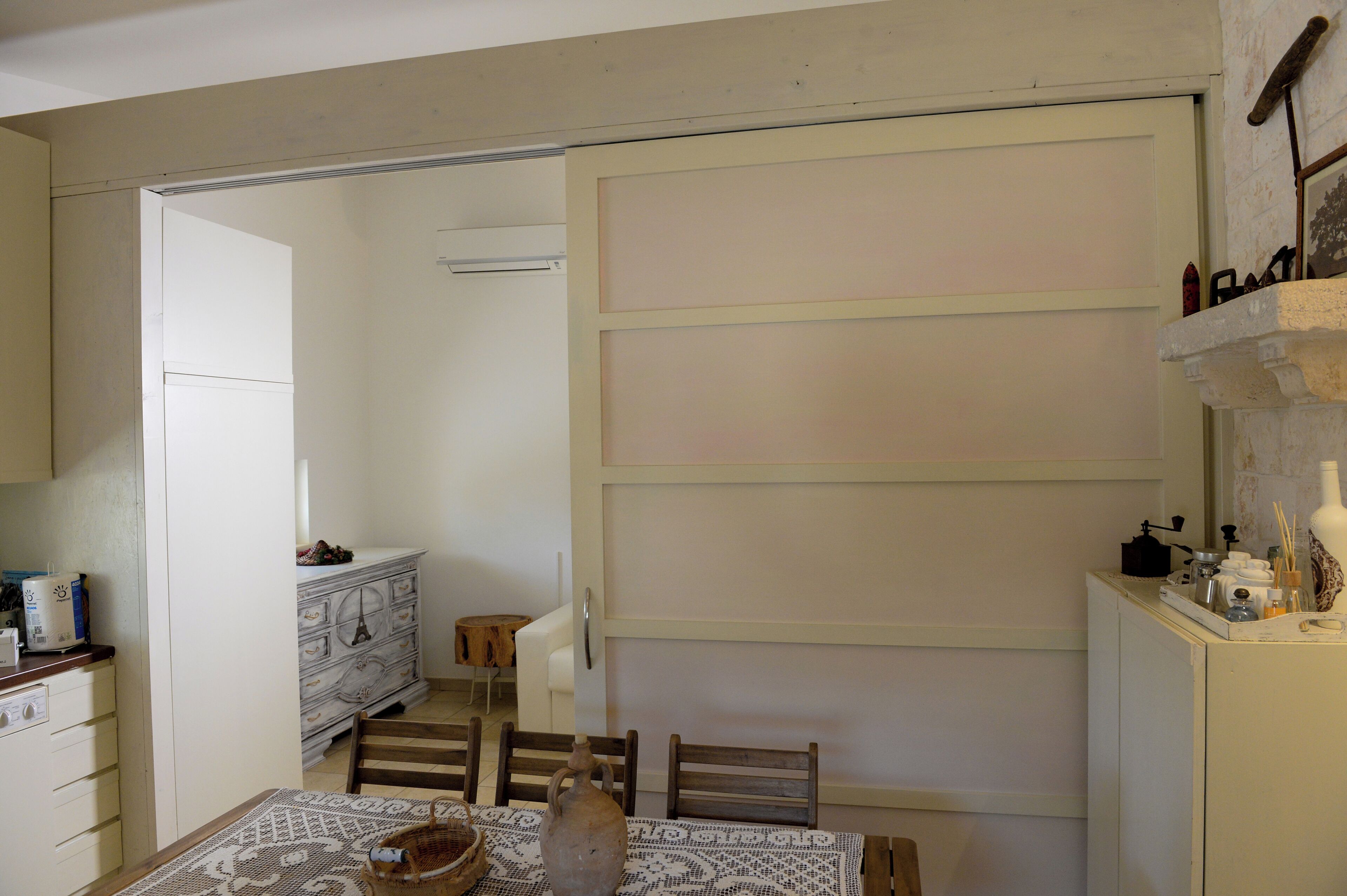 A compact kitchen with a dining table, chairs, a white cabinet, and a small wooden stool.