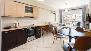 A modern kitchen with dark cabinets, a stove, and a dining area with a table and chairs. - Kalamata City Nest Ypapanti Cozy Bright Getaway (Kalamata)