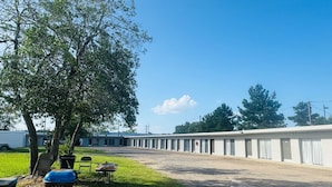 A motel with a row of rooms, a grassy area with a barbecue grill, and a tree. - holiday motel (Springhill)
