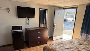A hotel room with a bed, a desk with a microwave, a TV, and a door leading to a parking area. - holiday motel (Springhill)