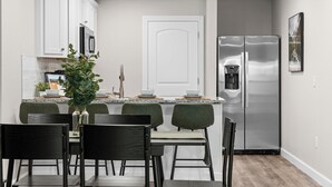 Une cuisine moderne avec des meubles blancs, un réfrigérateur en acier inoxydable et un coin repas avec des chaises vertes et une table.