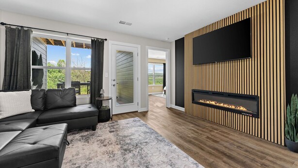 Un salon moderne avec un canapé d’angle, un téléviseur à écran plat fixé sur un mur recouvert de panneaux en bois et une cheminée intégrée.