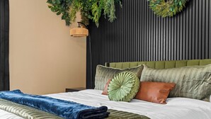 Un lit bien fait, avec une couette verte et blanche, une couverture bleue et plusieurs oreillers.