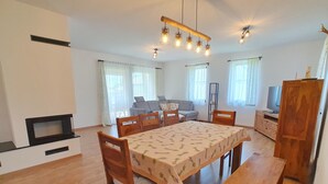 Un comedor con mesa y sillas de madera, un banco, un mueble para televisión y un sofá al fondo.
