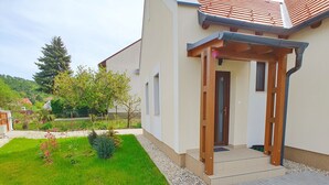 Una casa moderna con entrada pavimentada, una pérgola de madera y césped cuidado.