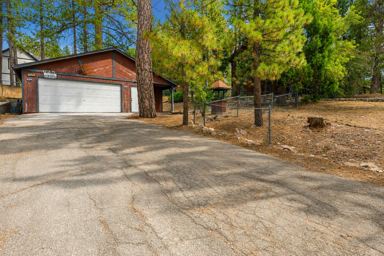 Une allée menant à une maison en bois et à un garage, le tout entouré de pins.
