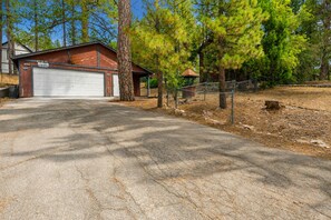 Una strada privata conduce a un garage con una casa in legno, immersa tra pini.