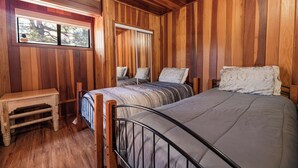 A wooden-paneled room with two beds, a small table, and a window. - Silver Rays (Big Bear Lake)